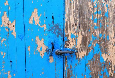 The primary subject of the image is a blue door with a rusty lock. The setting is a wooden door, and the visual style is a photo. The dominant colors are blue and rust, creating a mood of aged and worn-out appearance.