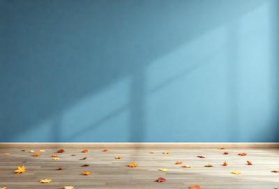 The primary subject of the image is a wooden floor with a scattering of leaves on it. The setting is a room with a blue wall, and the visual style appears to be a photo. The dominant colors are blue and orange, creating a warm and inviting atmosphere.