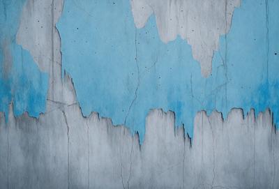 The primary subject of the image is a blue wall with peeling paint, giving it a worn and aged appearance. The setting is a room with a blue wall, and the visual style is a close-up of the wall. The dominant colors are blue and white, creating a calm and serene atmosphere.