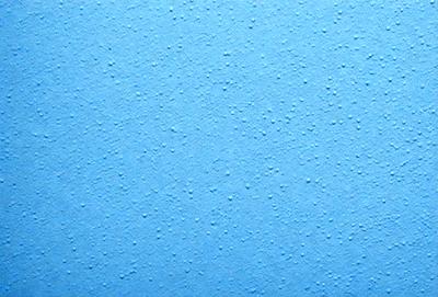 The primary subject of the image is a blue wall with a pattern of small dots. The setting is a room with a blue wall, and the visual style is a close-up of the wall. The colors and mood of the image are predominantly blue, creating a calm and serene atmosphere.