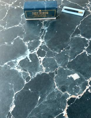 The primary subject of the image is a bottle of Aqua Marine soap, which is placed on a countertop. The setting is a countertop with a marble surface, and the visual style is a photo. The dominant colors in the image are black and white, giving it a classic and elegant appearance.