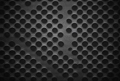 The primary subject of the image is a pattern of small circles, which are arranged in a dense and intricate manner. The setting is a black background, which contrasts with the circles, making them stand out. The visual style is a close-up of the pattern, showcasing the details of the circles. The colors and mood of the image are predominantly dark, with the small circles being the main focus and source of visual interest.