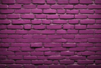 The primary subject of the image is a purple brick wall. The setting is a brick wall, and the visual style is a photo. The dominant colors are purple and pink, creating a warm and inviting atmosphere.