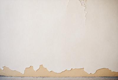 The primary subject of the image is a wall with peeling paint. The setting is a room with a white wall, and the visual style is a photo. The colors and mood of the image are predominantly white, giving it a clean and minimalist appearance.
