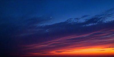 The primary subject of the image is a beautiful sunset with a vibrant orange sky. The setting is a cloudy sky, and the visual style is a photo. The colors and mood of the image are warm and serene, creating a captivating and peaceful atmosphere.