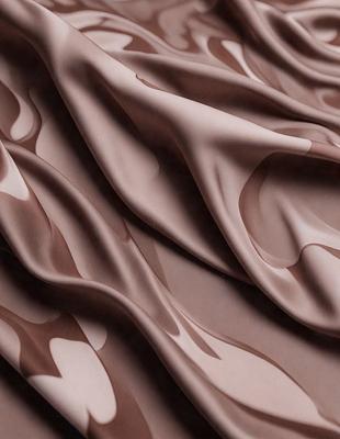 The primary subject of the image is a piece of fabric, which is the main object, scene, or focus of the image. The setting or background of the image is a brown surface, possibly a table or a wall. The visual style of the image is a close-up of the fabric, showcasing its texture and details. The colors and mood of the image are predominantly brown, giving it a warm and earthy atmosphere.