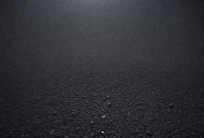 The primary subject of the image is a black surface, which appears to be a road or pavement. The setting is an outdoor environment, with no visible background or backdrop. The visual style is a close-up of the black surface, showcasing its texture and appearance. The colors in the image are predominantly black, giving the scene a dark and moody atmosphere.