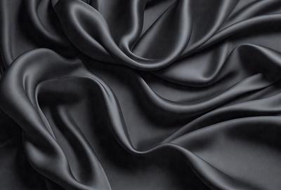 The primary subject of the image is a close-up of a black fabric, possibly a piece of clothing or a curtain. The setting is a dark background, which emphasizes the fabric's texture and pattern. The visual style appears to be a photo, as it captures the details of the fabric. The colors and mood of the image are predominantly dark, with the black fabric being the main focus.