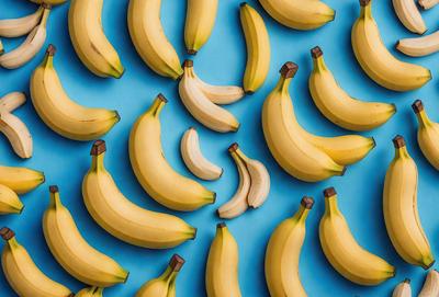 The primary subject of the image is a large number of bananas, which are arranged in a pattern on a blue surface. The bananas are of various sizes and are spread across the entire image. The visual style of the image is a close-up of the bananas, showcasing their details and textures. The colors and mood of the image are predominantly yellow, which is the color of the bananas, and blue, which serves as the background color. The overall atmosphere of the image is vibrant and fresh