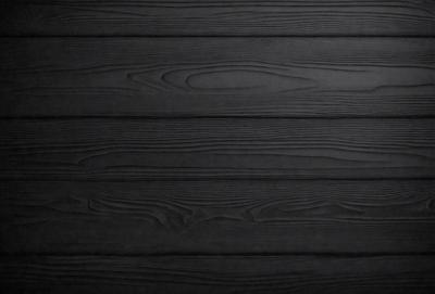 The primary subject of the image is a wooden wall with a black color. The setting is a room with a black background. The visual style is a close-up of the wooden wall, which gives a sense of texture and pattern. The colors and mood of the image are dark and moody, creating a dramatic atmosphere.