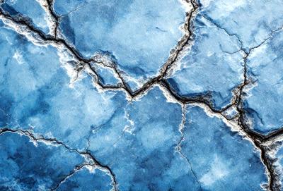 The primary subject of the image is a cracked blue surface, which appears to be a piece of a broken blue wall. The setting is a blue sky, and the visual style is a close-up of the cracked surface. The colors and mood of the image are predominantly blue, creating a calm and serene atmosphere.