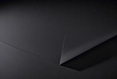 The primary subject of the image is a black piece of paper with a triangle shape cut out of it. The setting is a dark background, which contrasts with the paper. The visual style is a close-up of the paper, showcasing the triangle cutout. The colors and mood of the image are predominantly dark, with the black paper and the dark background creating a moody atmosphere.