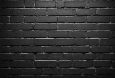 The primary subject of the image is a brick wall. The setting is a dark room, and the visual style is a black and white photo. The dominant colors are black and white, creating a moody atmosphere.