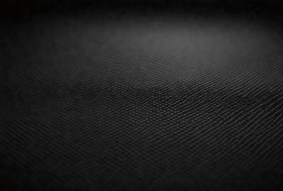 The primary subject of the image is a black background with a patterned texture. The setting is a dark room, and the visual style is a close-up of the patterned surface. The colors and mood of the image are predominantly dark and moody, with the black background and patterned texture creating a dramatic and mysterious atmosphere.