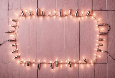 The primary subject of the image is a string of lights, which are illuminated and hanging from a wooden surface. The setting is a wooden wall, and the visual style appears to be a photo. The colors and mood of the image are warm and inviting, with the lights creating a cozy atmosphere.