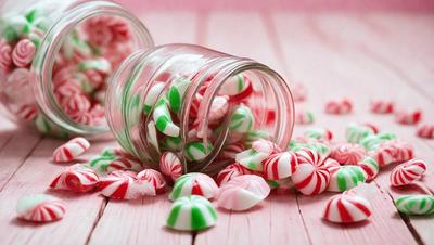 The primary subject of the image is a glass jar filled with candy canes. The jar is placed on a pink surface, which adds a warm and festive touch to the scene. The candy canes are predominantly green and white, creating a visually appealing and colorful display. The overall atmosphere of the image is cheerful and festive, as it showcases a popular holiday treat.