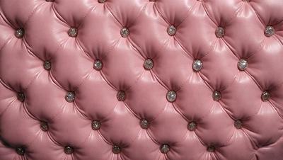 The primary subject of the image is a pink couch with a patterned design. The setting is a room with a pink background. The visual style is a close-up of the couch, showcasing its unique design. The colors and mood of the image are predominantly pink, creating a warm and inviting atmosphere.