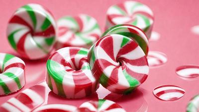 The primary subject of the image is a close-up of a candy cane, which is a popular Christmas treat. The candy cane is green, red, and white, and it is placed on a pink surface. The setting appears to be a table or countertop, and the visual style is a close-up, which emphasizes the details of the candy cane. The colors and mood of the image are festive and cheerful, as the candy cane is a symbol of the holiday season