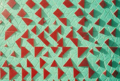 The primary subject of the image is a pattern of red triangles on a green background. The setting appears to be a wall or a surface with a tiled appearance. The visual style of the image is a combination of digital art and illustration, creating a unique and eye-catching design. The dominant colors in the image are red and green, with the red triangles standing out against the green background. The overall atmosphere of the image is vibrant and engaging, likely intended to draw attention and create a visually appealing environment