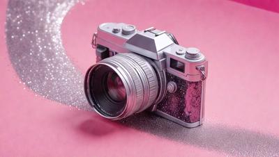 Primary subject: A silver camera with a pink background.

Setting/background: The camera is placed on a pink surface, which could be a table or a background.

Visual style: The image is a photo of the camera on the pink surface.

Colors and mood: The camera has a silver color, and the pink surface creates a warm and inviting atmosphere.