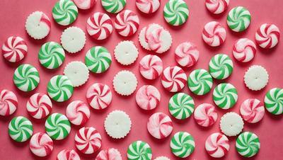 The primary subject of the image is a large number of candy canes, which are white and red in color. They are arranged in a visually appealing manner, covering the entire image. The setting is a pink background, which adds a contrasting color to the scene. The visual style of the image is a close-up of the candy canes, showcasing their details and textures. The overall atmosphere of the image is festive and joyful, as the candy canes are commonly associated with the hol