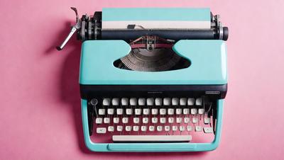 The primary subject of the image is a blue and white typewriter. The setting is a pink background, which adds a contrasting color to the scene. The visual style is a close-up of the typewriter, showcasing its details. The colors and mood of the image are predominantly blue and white, giving it a classic and nostalgic feel.