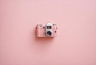 Primary subject: A pink camera.
Setting/background: A pink background.
Visual style: A photo.
Colors and mood: The pink camera and background create a warm and vibrant atmosphere.