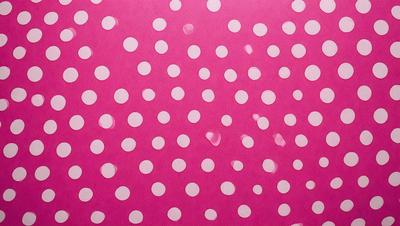 The primary subject of the image is a pattern of white polka dots on a pink background. The setting is a close-up of the polka dots, showcasing their intricate design. The visual style is a combination of a photo and digital art, as the polka dots are digitally created and placed on the pink background. The colors and mood of the image are predominantly pink and white, giving it a cheerful and playful atmosphere.