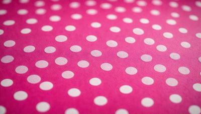 The primary subject of the image is a pink surface with a pattern of white polka dots. The setting is a close-up of the polka dot pattern, showcasing the intricate details of the dots. The visual style is a realistic representation of the polka dot pattern, with no indication of digital art or illustration. The colors and mood of the image are predominantly pink and white, creating a warm and inviting atmosphere.