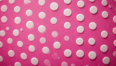 The primary subject of the image is a pattern of white dots on a pink background. The dots are arranged in a circular pattern, creating a visually appealing and unique design. The setting is a pink surface, which serves as the background for the dots. The visual style of the image is a combination of digital art and illustration, as the dots are created using a digital medium. The colors and mood of the image are predominantly pink and white, giving it a warm and inviting atmosphere.