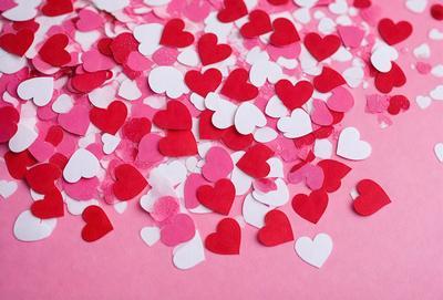 The primary subject of the image is a pile of red and white hearts. The hearts are scattered across a pink surface, creating a visually appealing and playful scene. The setting appears to be a creative and artistic environment, possibly a crafting or design workspace. The visual style of the image is a combination of digital art and illustration, with the hearts being crafted to resemble real hearts. The dominant colors in the image are red and white, creating a warm and inviting atmosphere.