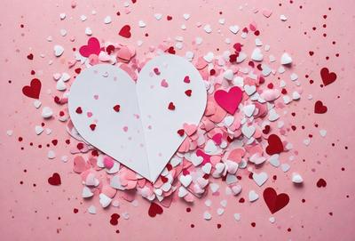 The primary subject of the image is a heart-shaped paper cutout, which is placed on a pink background. The heart is surrounded by a variety of pink and red hearts, creating a visually appealing and romantic scene. The visual style of the image is a combination of photo and digital art, as the heart is a cutout from a paper, and the background is pink. The colors and mood of the image are predominantly pink and red, which are often associated with love and affection.