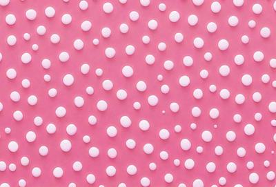 The primary subject of the image is a pattern of white dots on a pink background. The setting is a close-up of the pattern, showcasing the dots and their arrangement. The visual style is a combination of a photo and digital art, as the dots are arranged in a way that resembles a digital design. The colors and mood of the image are predominantly pink and white, creating a clean and simple aesthetic.