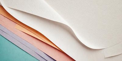 The primary subject of the image is a stack of different colored papers. The setting is a table, and the visual style is a close-up of the papers. The colors and mood of the image are predominantly pink and white, giving it a warm and inviting atmosphere.