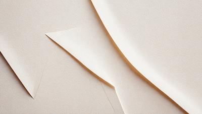 The primary subject of the image is a piece of paper, which is the main object, scene, or focus of the image. The paper is white and appears to be a piece of cardboard. The setting or background of the image is a table, which is visible in the foreground. The visual style of the image is a close-up, which highlights the details of the paper. The colors and mood of the image are neutral and calm, as the white paper creates a sense of simplicity and tranquility.