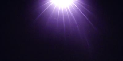 The primary subject of the image is a bright light source, possibly a star or a light bulb, shining in the dark. The setting is a night sky, with the light source being the main focus of the image. The visual style appears to be a photo, as the light source is captured in a clear and detailed manner. The colors and mood of the image are predominantly dark, with the bright light source standing out against the black background.