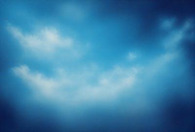 The primary subject of the image is a cloudy blue sky. The setting is a vast expanse of the sky, with no visible land or other objects. The visual style is a natural, outdoor scene. The colors and mood are predominantly blue and serene, with a hint of calmness.