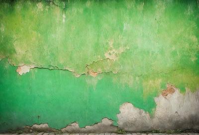 The primary subject of the image is a green wall with peeling paint. The setting is an outdoor environment, and the visual style appears to be a photo. The dominant colors are green and white, with the green wall being the main focus of the image. The overall atmosphere is somewhat deteriorated due to the peeling paint, but the green color adds a touch of freshness to the scene.