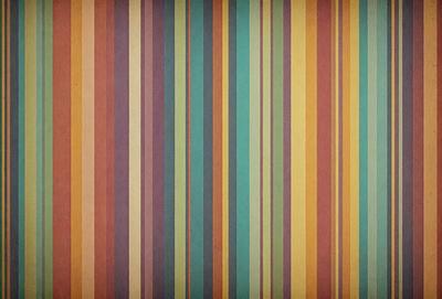 The primary subject of the image is a striped pattern, which is displayed on a wooden surface. The setting is a room with a wooden floor, and the visual style appears to be a combination of a photo and a pattern. The dominant colors in the image are orange, green, and blue, creating a vibrant and lively atmosphere.