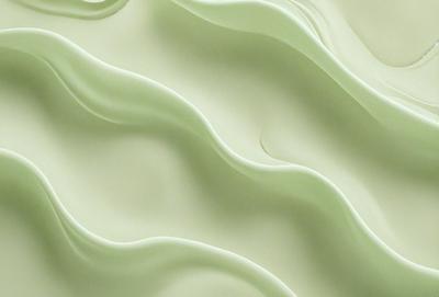 The primary subject of the image is a close-up of a green, swirling, and flowing substance, which appears to be a creamy or frothy material. The setting is a white background, which contrasts with the green substance. The visual style is a close-up, which emphasizes the details of the swirling material. The colors and mood of the image are predominantly green, giving it a soothing and natural atmosphere.