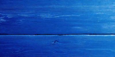 The primary subject of the image is a wooden surface, possibly a table or a wall, with a blue color. The setting appears to be a room with a blue wall, and the visual style is a close-up of the wooden surface. The colors and mood of the image are predominantly blue, creating a calm and serene atmosphere.