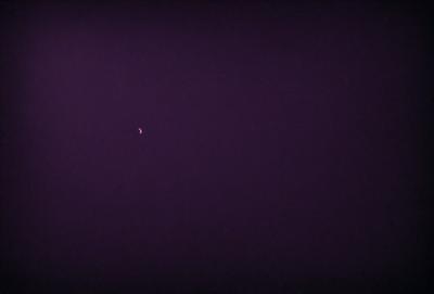 The image features a purple sky with a single moon visible in the distance. The moon is positioned towards the left side of the sky, and it appears to be the main subject of the image. The purple sky creates a serene and peaceful atmosphere, making the moon stand out as the focal point of the scene.