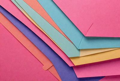 The primary subject of the image is a stack of colorful paper, which includes a variety of colors such as pink, yellow, blue, and purple. The setting is a pink background, which adds a vibrant and lively atmosphere to the scene. The visual style of the image is a close-up of the paper, showcasing the intricate details of the colors and patterns. The overall mood of the image is cheerful and lively, as the colorful paper creates a sense of joy and creativity