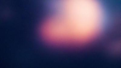 The primary subject of the image is a pink, purple, and orange cloud. The cloud is floating in a dark blue sky, creating a striking contrast between the cloud and the background. The visual style of the image is a photo, capturing the beauty of the cloud in its natural environment. The colors and mood of the image are vibrant and lively, with the pink and purple hues evoking a sense of warmth and the orange hues adding a touch of energy to the scene.