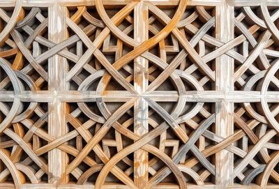 The image features a wooden lattice design with a variety of patterns and shapes. The primary subject is the intricate wooden lattice, which is the main focus of the image. The setting is a wooden wall, and the visual style is a close-up of the lattice design. The colors and mood of the image are warm and inviting, with the wooden lattice creating a sense of texture and depth.