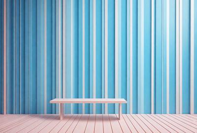 The primary subject of the image is a wooden bench. The bench is placed on a wooden floor, which is the setting for the scene. The visual style of the image is a photo, capturing the bench and its surroundings. The colors and mood of the image are predominantly blue, creating a calm and serene atmosphere.