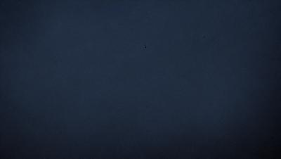 The primary subject of the image is a dark blue sky with no clouds. The setting is a vast, open space with no visible landmarks or objects. The visual style is a black and white photo, which adds a sense of timelessness and simplicity to the scene. The colors and mood are predominantly dark and moody, with the absence of clouds and the vastness of the sky contributing to the overall atmosphere.