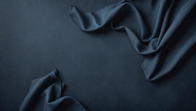 The primary subject of the image is a blue cloth, which is draped over a dark blue background. The setting appears to be a room with a table, and the visual style is a close-up of the cloth. The colors and mood of the image are predominantly dark and moody, with the blue cloth being the main focus.