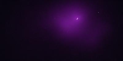 The primary subject of the image is a purple moon, which is the main object in the scene. The setting is a dark, purple sky, creating a moody atmosphere. The visual style is a photo, capturing the moon and its surroundings. The colors and mood of the image are predominantly purple, giving it a mysterious and serene appearance.