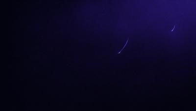 The primary subject of the image is a long, thin line or tail, which appears to be a part of a larger object. The setting is a dark, purple background, which creates a moody atmosphere. The visual style of the image is a combination of a photo and a drawing, giving it a unique and artistic appearance. The colors and mood of the image are predominantly dark and mysterious, with the purple background adding to the overall ambiance.